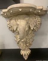 Front view of the sandstone color elephant head wall sconce showing detailed elephant face and decorative leaf elements below.