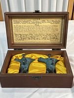 Photo of two bronze chüeh wine vessels displayed in a wooden box with yellow silk lining and a multilingual descriptive plaque above them.