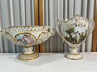 Front view of both porcelain vases showing overall shape, hand-painted cherubs, nature scenes, gold accents, and Rococo Revival style detailing.
