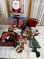 Full view of Christmas decorations including Santa plush, basket, ornaments, snow globe, decorative tree topper, and other decorations arranged on a table.