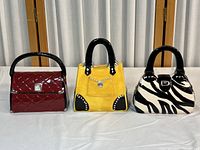 Front view of three ceramic purse coin banks: red, yellow, and zebra print styles.