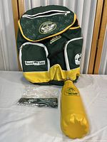Front view of Oakland Athletics Kids Club green/yellow backpack with two front zippered pockets, 'Round Table' patch, and two accessories placed in front