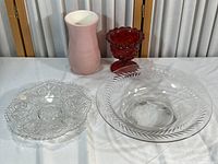 Four items displayed: pink ceramic vase, red diamond cut glass vase, clear cut glass dish, clear bowl with leaf etching.
