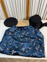 Photo of three wool hats (black beret, tan flat cap, black decorated hat) and blue floral kimono skirt.