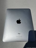 Back view of Apple iPad showing silver aluminum body, Apple logo, iPad branding, minor edge dent on top corner.
