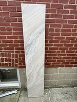 Full view of the white marble slab standing upright against a brick wall, highlighting its size and beveled edges.