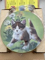 Front view of collector plate showing kitten and floral design with signature Sadako Mano.