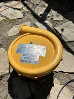 Top angled view of yellow plastic electric air blower fan outdoors showing curved exhaust outlet and surface scratches.