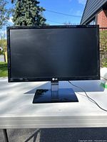 Front view of LG monitor on white table under daylight outdoors, showing the screen and front stand base with LG logo below display edge.