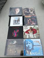 Top-down photo of 8 assorted music CDs arranged in two columns on concrete surface