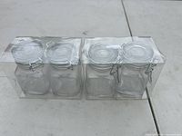 Four small glass storage jars in secure plastic packaging, showing the top view with metal clamp lids.