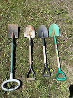 Four used garden shovels with different handle styles laid out on grass, showing rust and wear on blades.