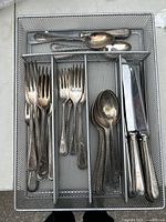 Flatware set arranged in a divided tray showing spoons, forks, and knives with beaded edge pattern and some wear.