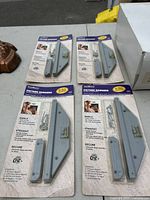 Top-down view of four TrackMaster picture hanger sets in original packaging, showing metal hangers, wood adapters, and installation hardware.