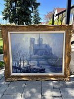 Front view of the framed painting showing Notre Dame Cathedral scene with river and boats, ornate gold wood frame.