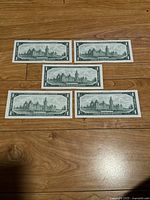 Five Canadian one dollar banknotes laid out showing their backs with the Parliament buildings.