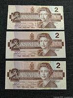 Three 1986 Canadian two dollar bills laid flat, showing the front side with Queen Elizabeth II portrait and denomination '2'