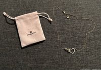 Full view of Swarovski Eternal Romance necklace laid out next to branded Swarovski pouch on dark fabric background.