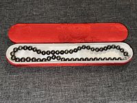 Black pearl necklace displayed inside open red decorative box with floral pattern.