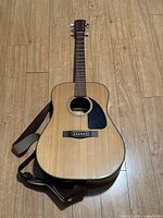Full view of the Fender acoustic guitar lying on wooden floor with attached leather strap.