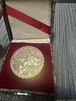Coin showing stylized Great Wall of China with architecture and cloud motifs, placed inside red velvet-lined presentation case with cream cushioned lid and red ribbon.