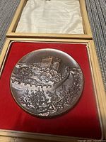 Photo of the medallion depicting the Great Wall of China on the obverse side in high relief, placed inside wooden box with red felt and satin lining.
