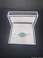 Silver bracelet with eye-shaped charm displayed inside white presentation box with foam padding.