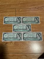 Front view of 5 Canadian 1967 Centennial one dollar banknotes showing Queen Elizabeth II portrait and denomination.