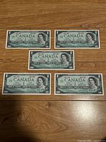 Front view of five Canadian one dollar bills from 1967 showing Queen Elizabeth II portrait and denomination.