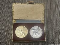 Two 1987 Chinese commemorative coins, one gold-tone and one silver-tone, inside a presentation box with a beige and maroon interior.