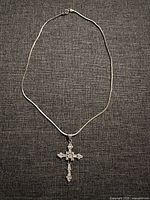 Full view of the silver chain necklace with cross pendant on fabric background.