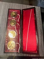 Closed view of four gold-tone commemorative medals in a red silk-lined presentation box, photographed from above.