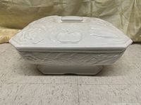 Side view of the white ceramic warming dish showing embossed vegetable patterns and rectangular shape with base.