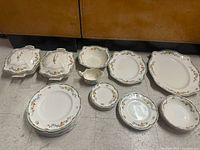 Photo showing multiple platters, serving bowls with lids, and various plates arranged on the floor with floral decorations and signs of wear.