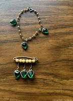 Photo showing the bracelet and bar brooch together on a wooden surface, highlighting the green heart-shaped charms and beadwork.
