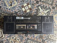 Top view of the Aiwa CA-DW95 boombox showing dual cassette decks, radio tuner, and speakers on patterned cloth background