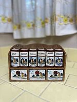 Front view of six ceramic spice jars in wooden rack with painted windmill scenes and labeled spices