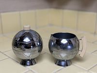 Side view of sugar bowl with lid and creamer with bakelite handle on tiled surface