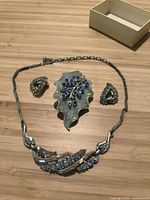 Photo showing vintage Coro jewelry set of brooch, earrings, and necklace with blue stones on a wood surface with a small box in background.