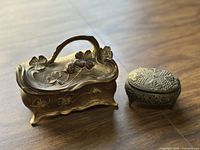 Photo of the two trinket boxes showing front and top view, details of clovers and flowers on larger box, embossed floral pattern on smaller box.