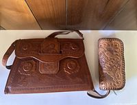 Photo showing a vintage brown leather purse with embossed floral and swirl patterns and a matching embossed leather wallet.