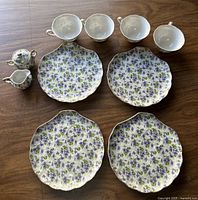 Full set layout showing four plates, four cups, sugar bowl with lid, and creamer jug with violet floral pattern on porcelain.