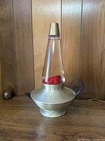 Full front view of genie lamp-shaped lava lamp on wood surface against paneled background.