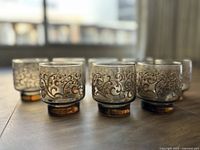 Four vintage Libbey Pardo hostess glasses with etched scroll and floral decor on grey glass supported by amber bases, side view showing design details.