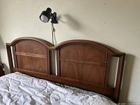 Full view of the vintage mid century wooden headboard mounted behind a bed with bedding and nearby wall-mounted lamp.