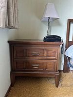 Mid-century style wooden nightstand with two drawers, brass handles, lamp and rotary phone on top