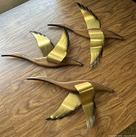 Three brass and wood duck wall art pieces on wooden surface, showing overall condition and design.
