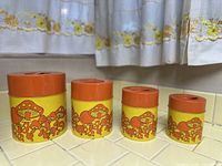 All four nesting canisters arranged largest to smallest on tiled counter beneath patterned curtain
