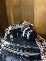 Three-quarter front view of Nikon camera with lens mounted, strap draped over soft case