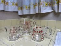 Three vintage Pyrex glass measuring cups arranged side-by-side showing the red measurement markings and glass construction.